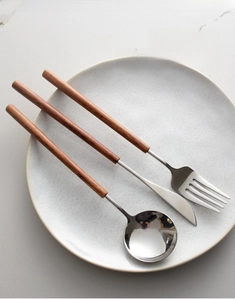 Minimalist 304 stainless steel cutlery set with pear wood handles on a ceramic plate