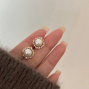 Detail von 14K vergoldeten Perlenohrringen mit Zirkonia-Halo in der Hand gehalten