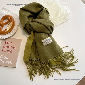 Detailed view of green cashmere-feel scarf with elegant long tassels and woven brand label