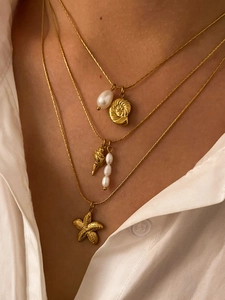 Close-up of layered gold necklace with seashell, starfish charms and freshwater pearls