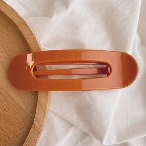 Close-up of a large orange matte duckbill hair clip on a wooden tray and white fabric