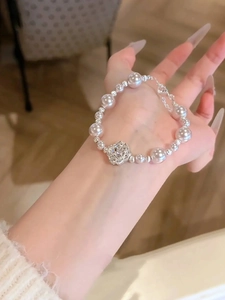 Détail d'un bracelet de perles avec breloque fleur porté au poignet chez soi