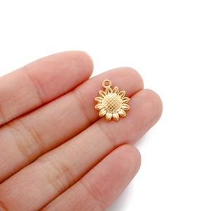Macro shot of a golden stainless steel sunflower charm pendant held on a fingertip