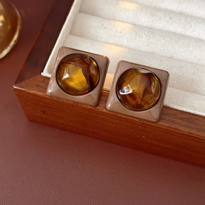 Close-up of square amber resin earrings with tortoiseshell texture on cream velvet lining