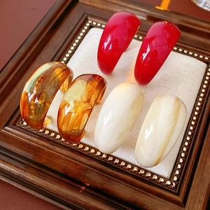 Detail view of retro C-shaped resin earrings in red, amber, and marble white on a tray