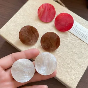 Three pairs of marble acrylic round stud earrings with gold glitter in red, brown, and white