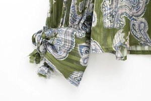 Macro detail of paisley print cuff with gold metallic threads on sheer green fabric