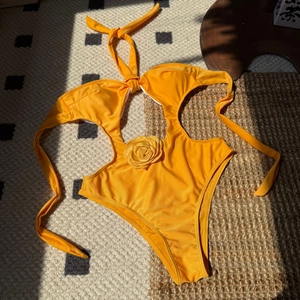 Detail of a bright orange one-piece swimsuit with cutout and handmade floral ornament