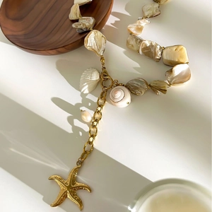 Starfish shell necklace with gold charms and natural mother of pearl beads on marble surface