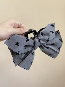 Dettaglio molletta per capelli in tessuto grigio con fiocco ricamato nero e base in plastica