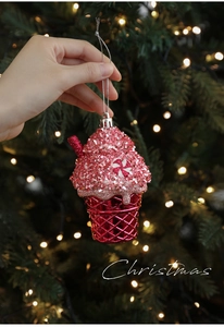 Pink glitter ice cream cone ornament held by hand against a festive Christmas tree background