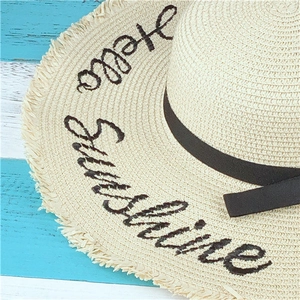 Detail of Hello Sunshine embroidery on straw hat with elegant black ribbon and frayed edges