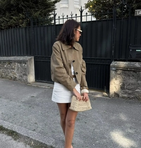 Detail of tan suede short jacket styled with a white skirt and a woven handbag
