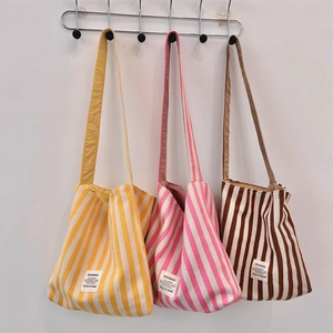 Tre borse tote in tela a righe nei colori giallo, rosa e marrone appese a ganci