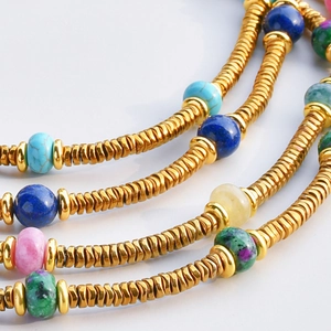 Colorful tourmaline beaded necklace with gold titanium wave spacers on white background