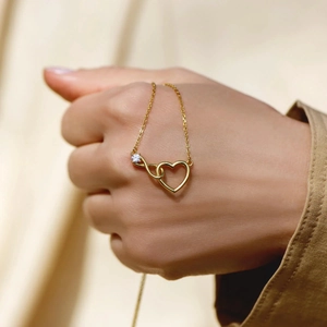 Gold s925 silver infinity heart necklace with white zircon held against silk background