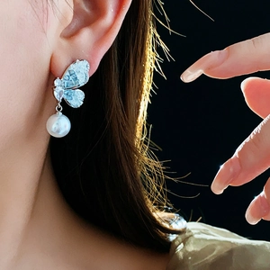 Detailed close-up of butterfly earrings with blue zircon wings and a round white pearl drop