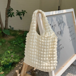 Detail of white bubble textured shoulder bag hanging on a wooden sign in a cafe garden