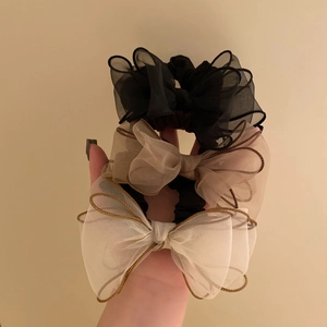 Detailed macro view of three organza bow scrunchies in black, beige, and champagne tones