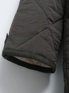 Macro shot of diamond quilted sleeves and ribbed knit cuffs on dark olive winter jacket