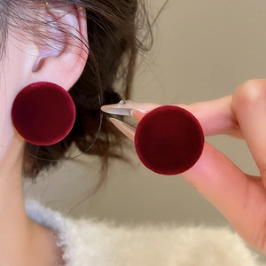 Close-up of deep red velvet round stud earrings worn on ear showing premium texture