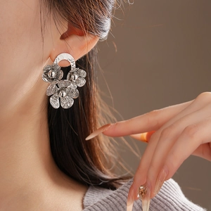 Detail of silver floral stud earring with hammered texture worn by a model