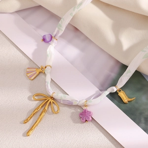 Detail der Blumenband-Halskette mit goldenem Bogen, Blumen- und Stiefelanhängern auf Stoff