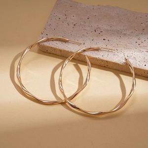 Detailed close-up of golden twisted geometric hoop earrings on a textured stone base