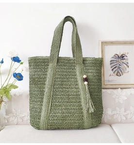 Green large woven straw tote bag with wood bead tassel in a cozy home setting