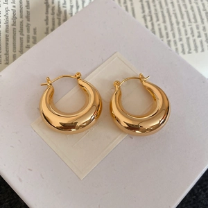 Boucles d'oreilles créoles C dorées sur un écrin blanc avec un livre en arrière-plan