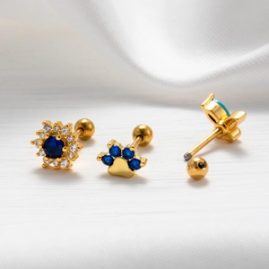 Macro detail of gold piercing studs featuring blue zircon flower and paw print designs