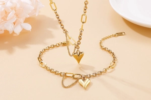Detailed view of a gold heart pendant bracelet with delicate chain on a beige background