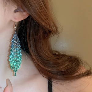 Detail of long feather drop earrings with blue-green gradient rhinestones on model