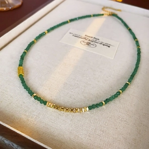 Détail de perles facettées vertes et d'une perle cylindrique en or sur un collier vintage