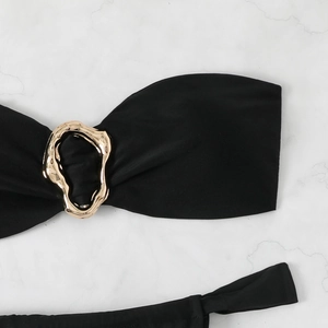 Detail of black bikini top featuring a central irregular gold metal ring on marble background