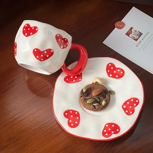 Top view of handmade ceramic coffee mug and saucer with red heart and dot patterns