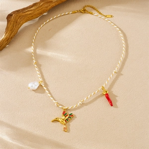 Detailed view of woven necklace with gold hummingbird, pearl and red chili pendants