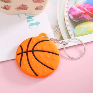 Close-up of orange silicone basketball keychain with silver metal ring on pink surface