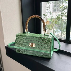 Detail of green crocodile texture handbag with bamboo handle and gold metal hardware