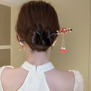 Close-up of wooden hair stick with red flower, golden leaves and tassel on back of head