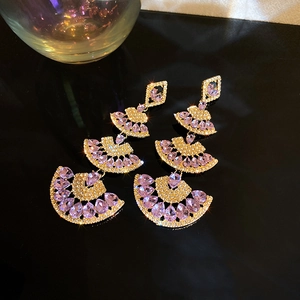 Macro shot of fan-shaped golden earrings featuring purple teardrop gems and rhinestones