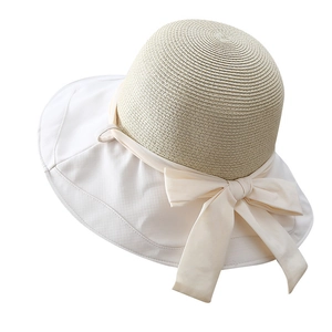Detail of summer straw sun hat with large beige fabric brim and decorative bow accent
