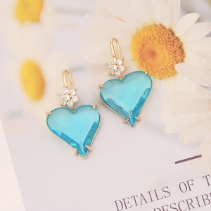 Macro detail of sky blue heart-shaped earrings with gold floral zircon accents