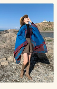Blue hooded ethnic poncho with red patterns worn on a sunny beach with sea background