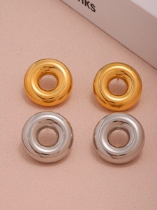 Detail of chunky gold and silver donut hoop earrings arranged on a soft pink surface