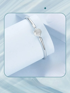 Detail showing silver open bangle featuring a delicate shell charm on a light blue background