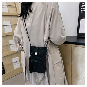 Détail du sac bandoulière noir avec texture plissée, perle et longue décoration de gland
