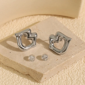 Polished silver hollow heart earrings on beige textured stone with silicone backings