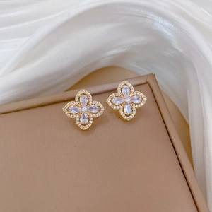 Macro shot of gold floral earrings with teardrop zircon petals on white silk background