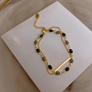 Détail d'un bracelet double chaîne dorée avec pierres ovales vertes, grises et barre fixe